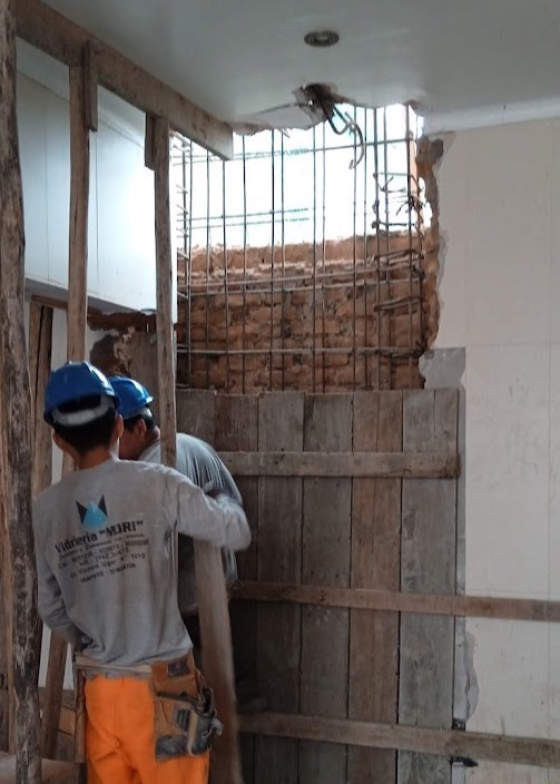Reforzamiento estructural en casa antigua de Miraflores por ARQBIMStudio, obreros realizando apuntalamiento de madera y colocación de armadura de acero para muro de ladrillo en remodelación sísmica.